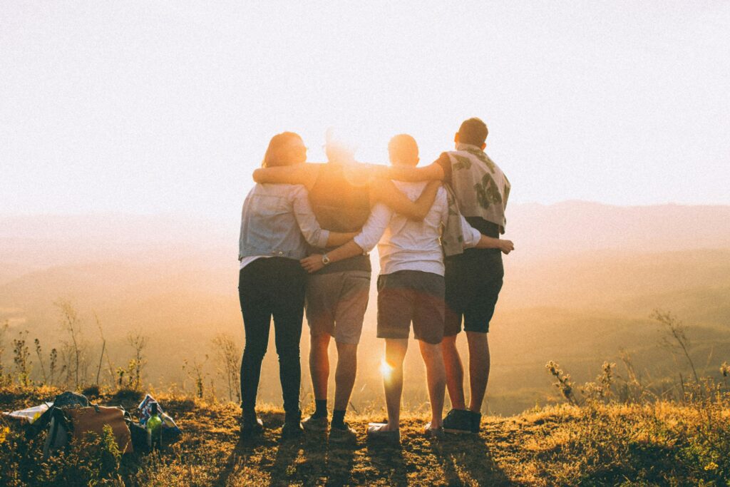 Group of friends standing together at sunset overlooking countryside landscape