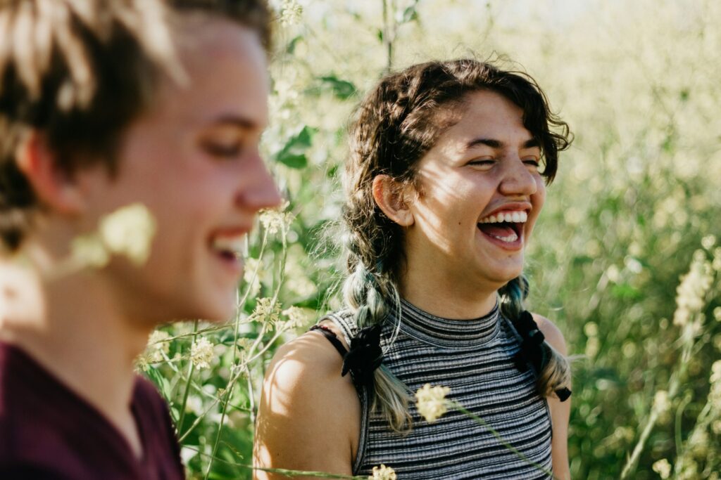 Two people laughing outdoors in a sunny wildflower field